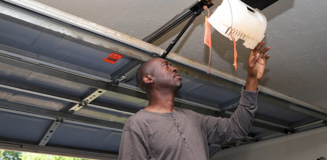 Man reaching up to inspect a ceiling-mounted garage door opener inside a residential garage.