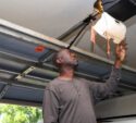 Man reaching up to inspect a ceiling-mounted garage door opener inside a residential garage.