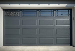 A closed dark gray garage door with rectangular panels and a row of small windows at the top.