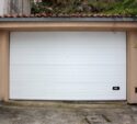 A closed white garage door set in a stone and stucco wall with a tiled roof, on a concrete driveway.