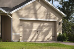 A beige single-car garage with a closed sectional door attached to a home