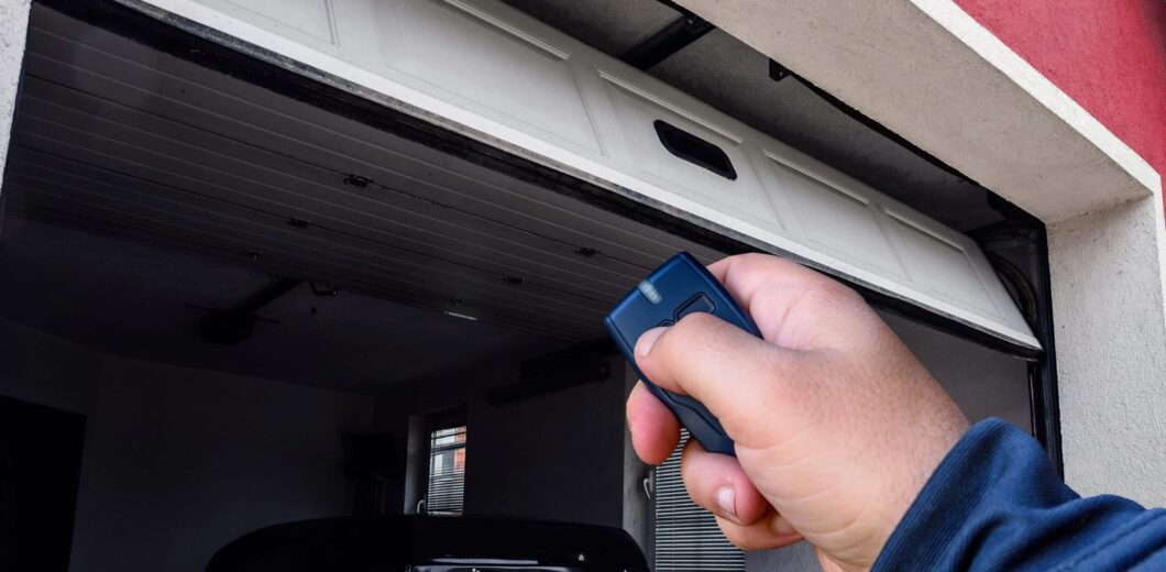A person uses a remote control to open a garage door, with a car parked inside the garage.
