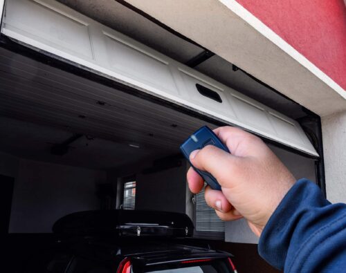 A person uses a remote control to open a garage door, with a car parked inside the garage.
