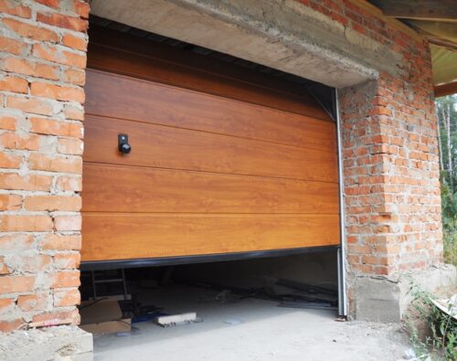 Partially open wooden garage door in a brick building under construction, with tools and materials visible inside the garage.
