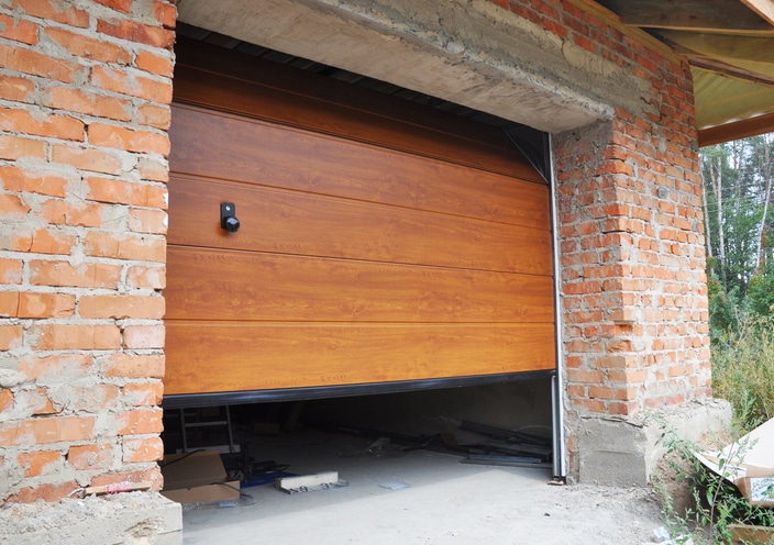 Partially open wooden garage door in a brick building under construction, with tools and materials visible inside the garage.