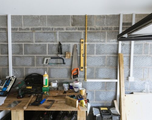 A workbench in a garage with various tools, glue, paint cans, and a spirit level on a brick wall.