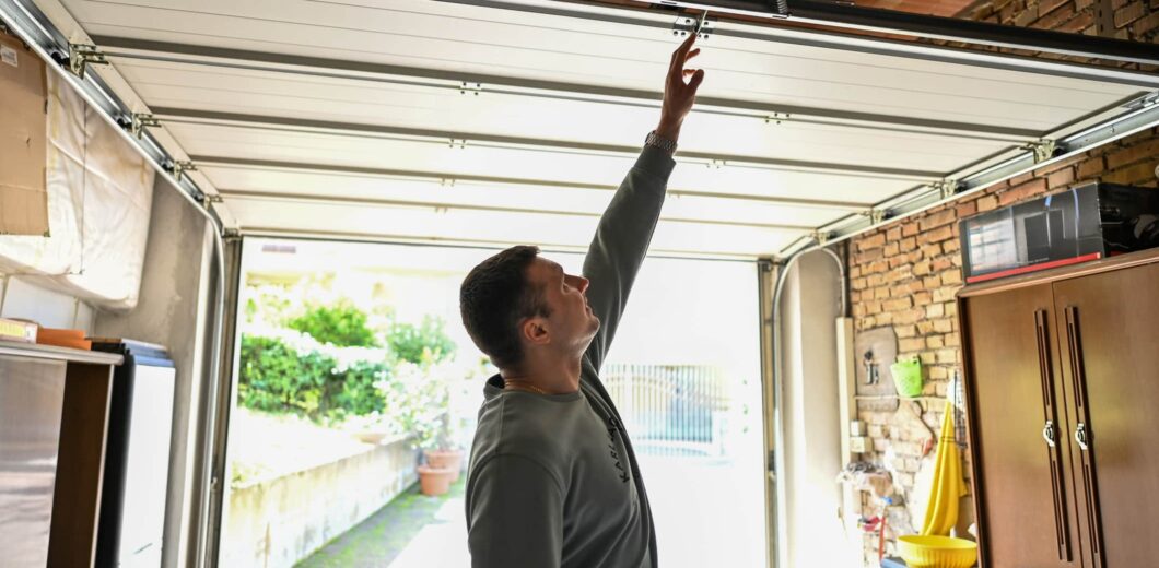 A man inside a garage reaches up to manually open or close a partially raised garage door.