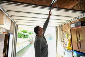A man inside a garage reaches up to manually open or close a partially raised garage door.