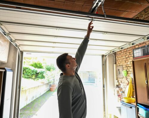 A man inside a garage reaches up to manually open or close a partially raised garage door.