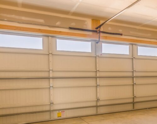 Interior view of a clean, empty garage with a closed sectional garage door featuring four rectangular windows near the top.
