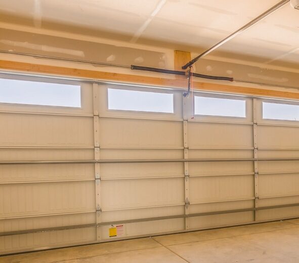 Interior view of a clean, empty garage with a closed sectional garage door featuring four rectangular windows near the top.