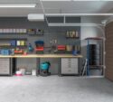 A clean, organized garage with workbenches, storage cabinets, tools on wall panels, a stack of tires, a vacuum, and the garage door partially open.
