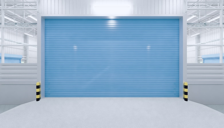 A closed blue industrial roll-up door with yellow and black safety bollards on each side in a clean, well-lit warehouse.