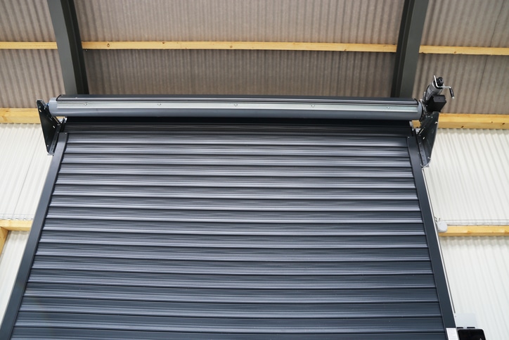A metal roller shutter door is partially open inside an industrial building with a corrugated roof and metal frame.