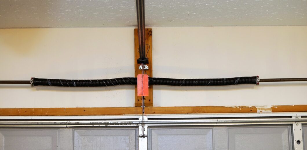 A broken, loose garage door torsion spring mounted above a closed gray garage door inside a garage.