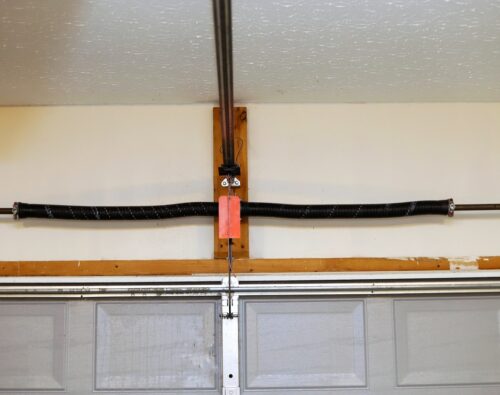 A broken, loose garage door torsion spring mounted above a closed gray garage door inside a garage.