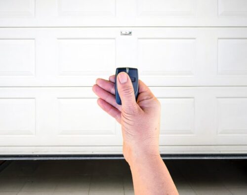 A hand holding a remote control in front of a closed white garage door.