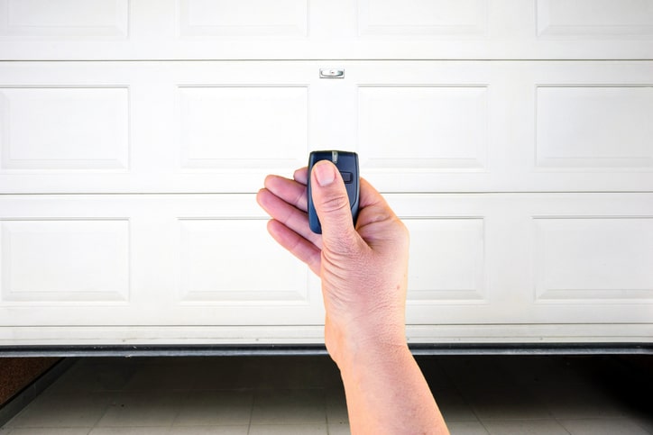 A hand holding a remote control in front of a closed white garage door.