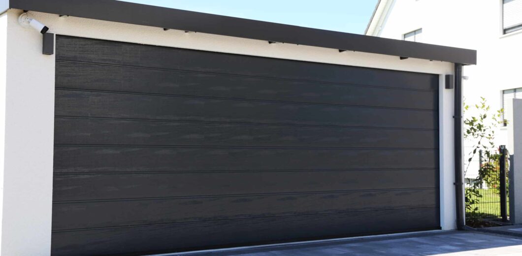 A closed, modern black garage door attached to a white building, with a paved driveway in front.