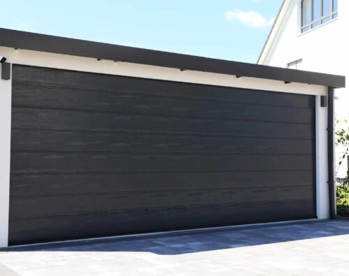 A closed, modern black garage door attached to a white building, with a paved driveway in front.