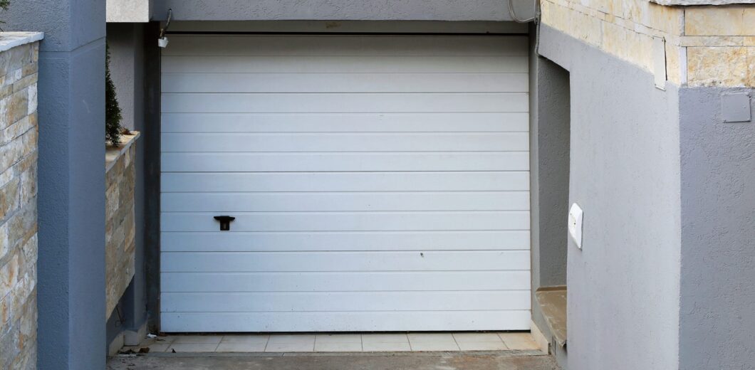 Closed white garage door set in a recessed concrete driveway, surrounded by gray and beige walls.