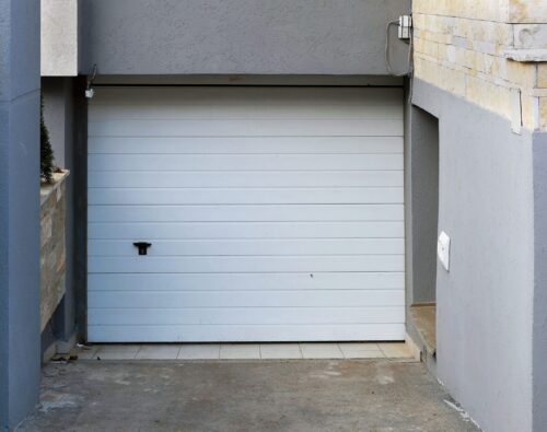 Closed white garage door set in a recessed concrete driveway, surrounded by gray and beige walls.