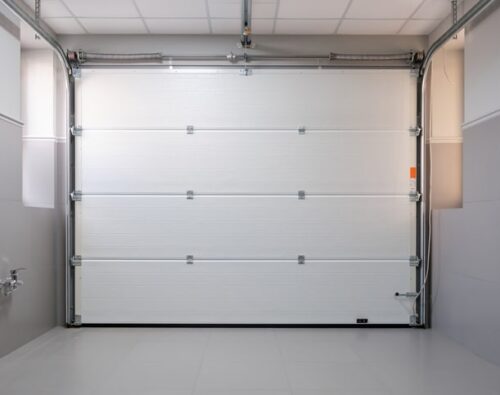 Closed white sectional garage door viewed from inside a clean, modern garage with tiled floor and gray walls.