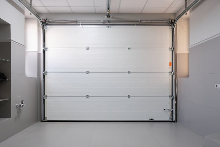 Closed white sectional garage door viewed from inside a clean, modern garage with tiled floor and gray walls.