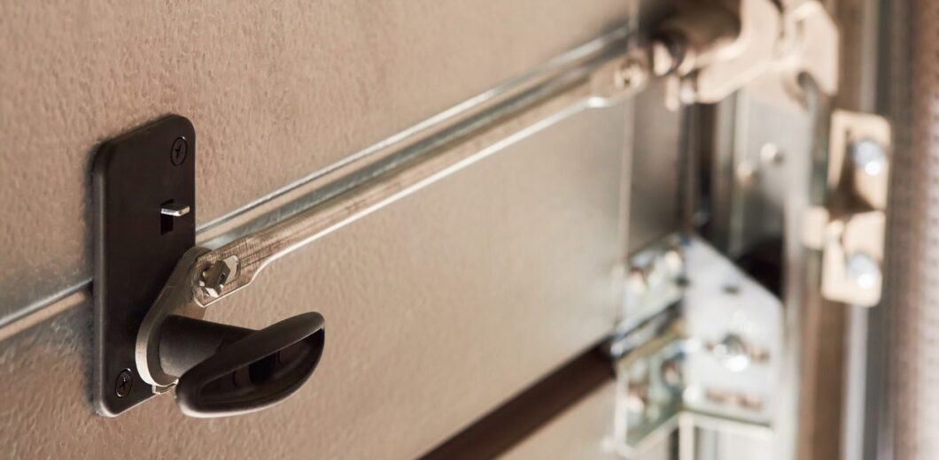 Close-up of a metal garage door lock mechanism with a handle and sliding bolt in the locked position.