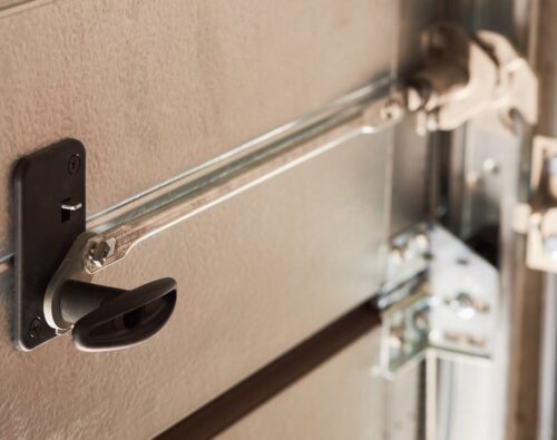 Close-up of a garage door lock mechanism with a black handle and metal rods securing the door.