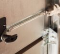 Close-up of a metal garage door lock mechanism with a black handle and connecting metal rod on a sectional door.