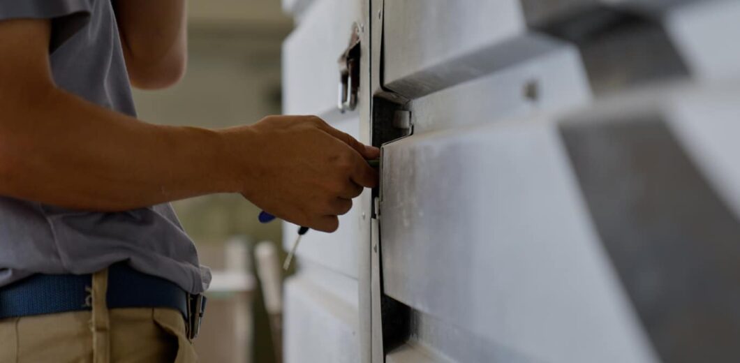 A person uses a tool to unlock or repair a metallic rolling shutter door.