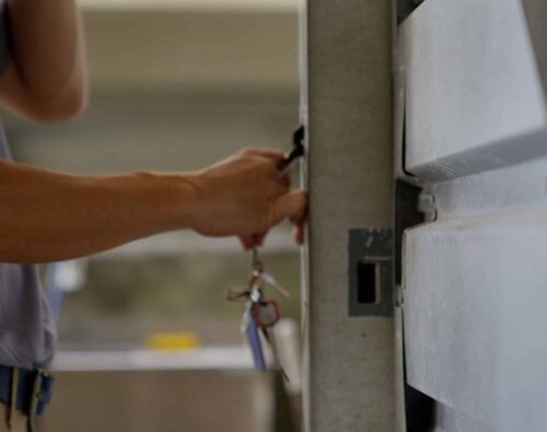 A person holds a set of keys and unlocks a metal door or cabinet with one hand.