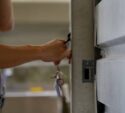 A person unlocking a metal door with a key, holding a set of keys in their hand.