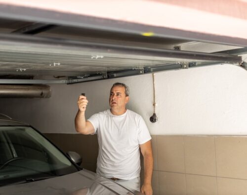 Man closing door in a garage with remote control, standing beside his car