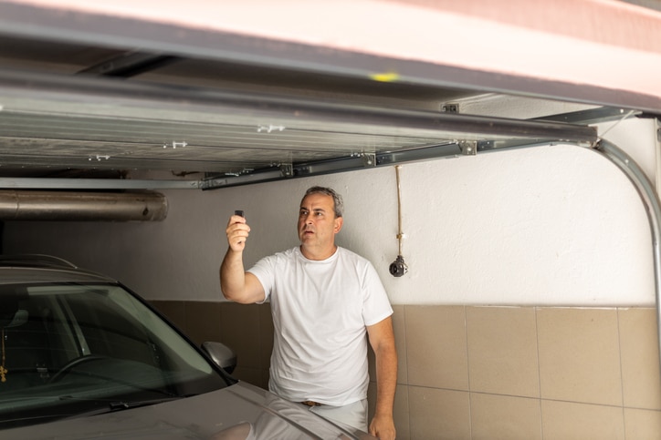 Man closing door in a garage with remote control, standing beside his car