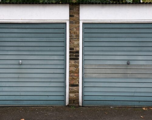 Two closed blue-grey garage doors set in a brick wall with white trim, viewed from the street.