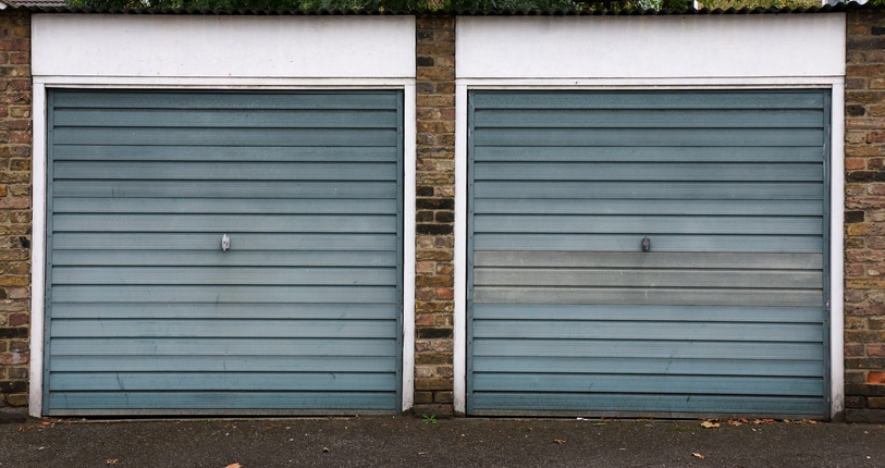 Two closed blue-grey garage doors set in a brick wall with white trim, viewed from the street.