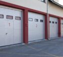 Four numbered garage doors, painted white with red borders, are seen in a row on the side of a building.