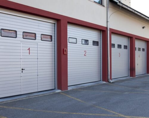 Four numbered garage doors, painted white with red borders, are seen in a row on the side of a building.