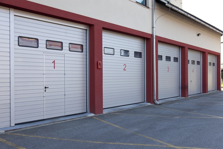 Four numbered garage doors, painted white with red borders, are seen in a row on the side of a building.