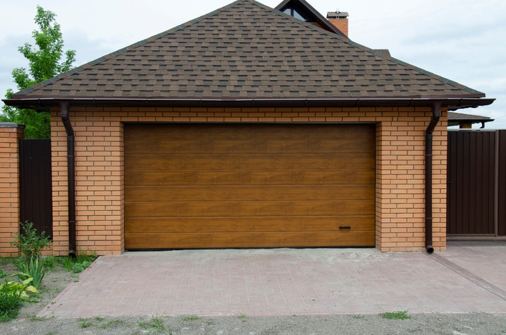 A closed wooden garage door set in a brick-walled garage with a paved driveway in front.