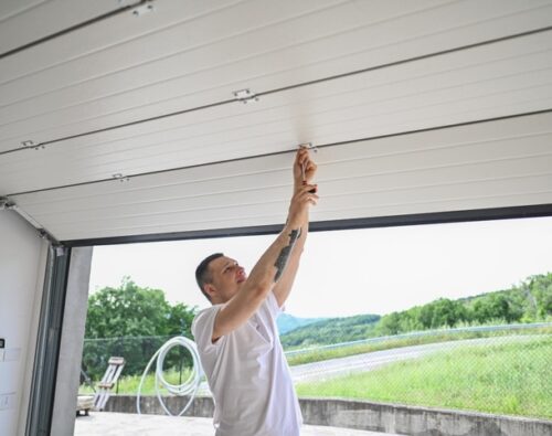 A person in a white shirt adjusts or repairs the inside of a partially open garage door during the daytime.