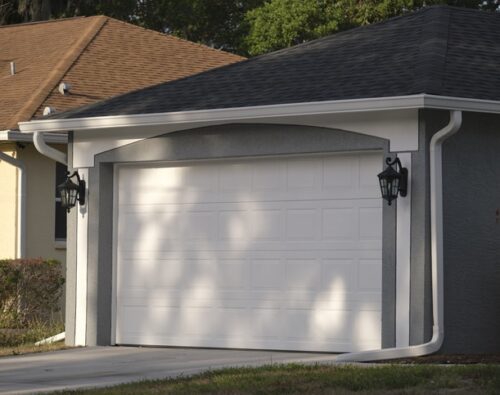 A closed white garage door on a suburban house with two black wall-mounted lanterns on either side.
