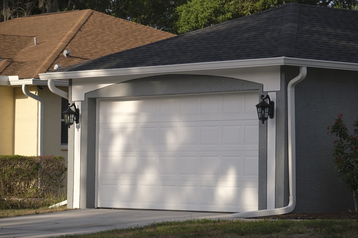 A closed white garage door on a suburban house with two black wall-mounted lanterns on either side.