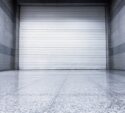 White rolling steel shutter door in a modern commercial space with polished concrete floor and gray stone walls.