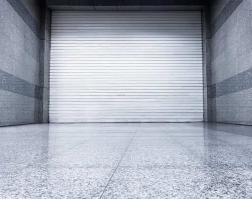 White rolling steel shutter door in a modern commercial space with polished concrete floor and gray stone walls.