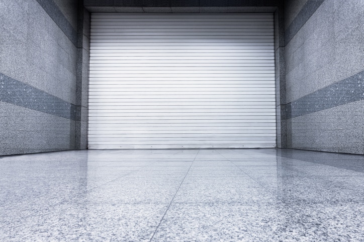 White rolling steel shutter door in a modern commercial space with polished concrete floor and gray stone walls.