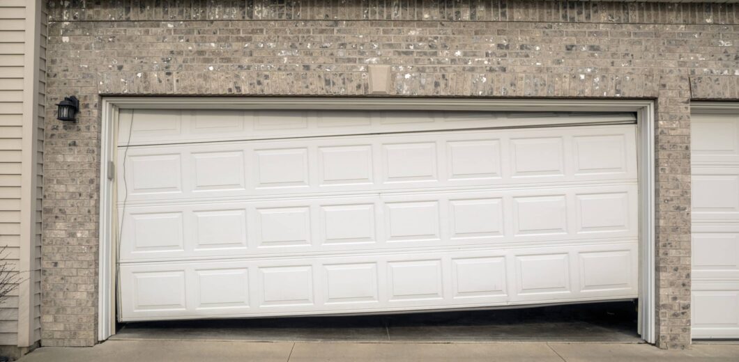 A white garage door is partially open and appears broken, sagging unevenly in the middle.