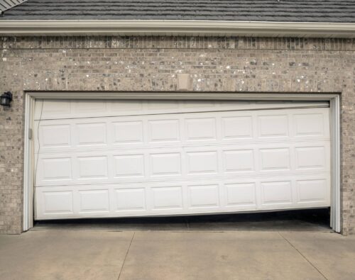 A white garage door is partially open and appears broken, sagging unevenly in the middle.